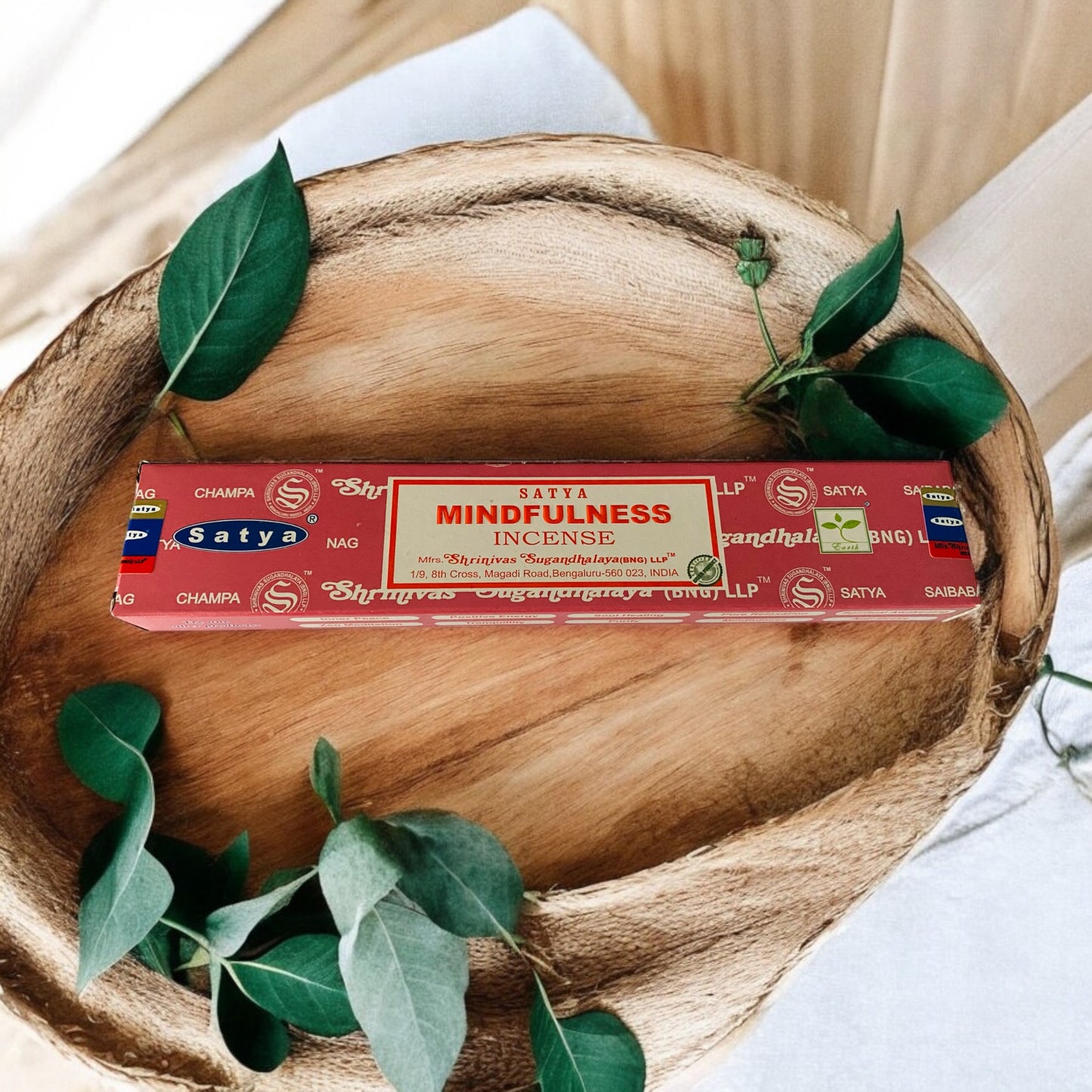 A package of Satya Mindfulness incense sticks placed on a wooden surface with green leaves around it, indicating a calming and meditative atmosphere.