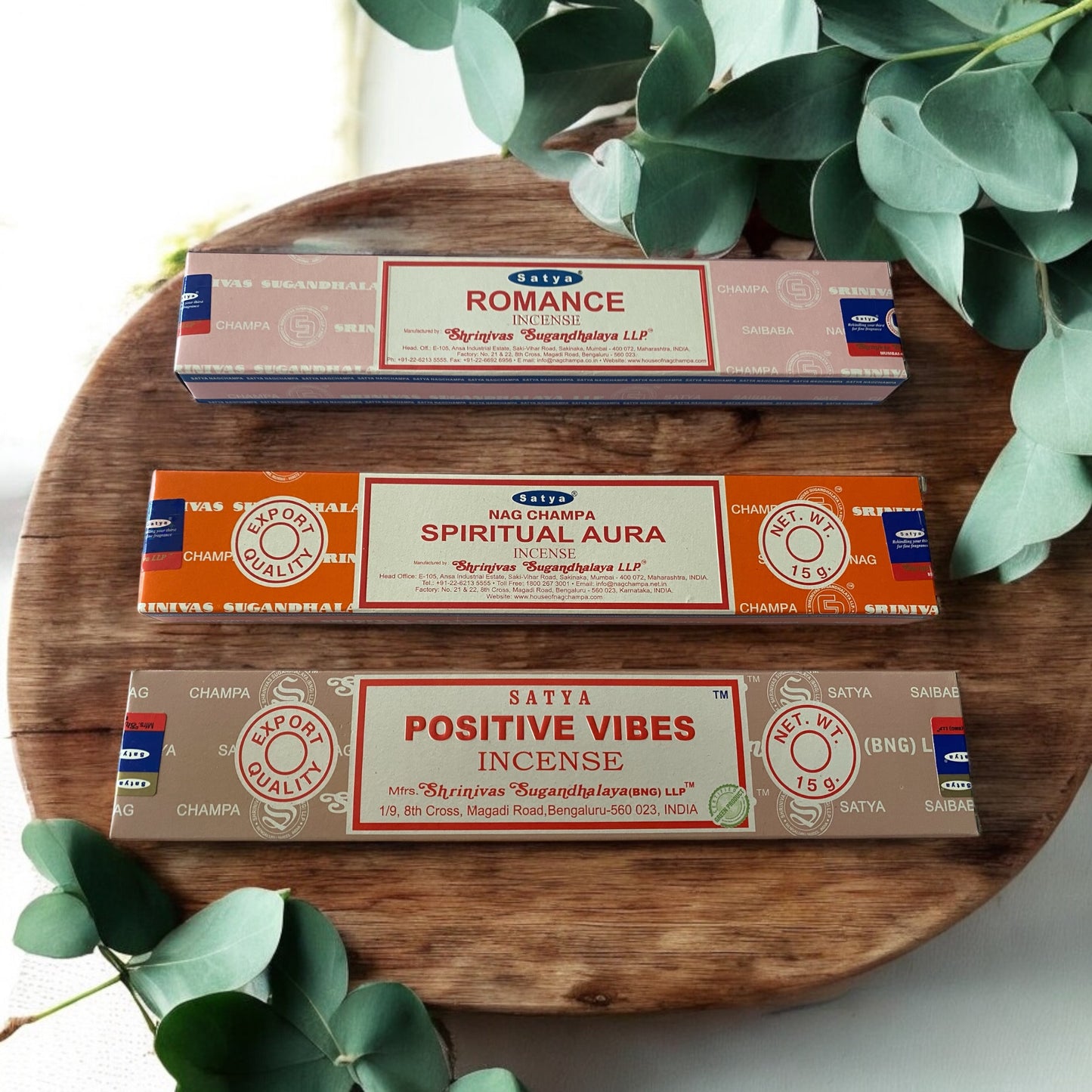 Three incense stick packs labeled 'Romance', 'Spiritual Aura', and 'Positive Vibes' placed on a wooden platter with green leaves in the background.