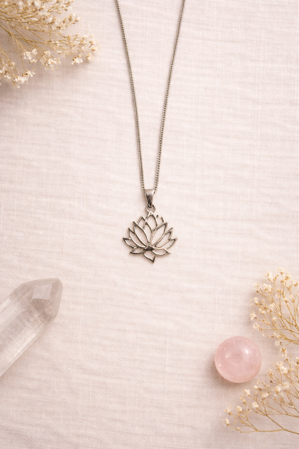 Lotus flower pendant necklace on a light pink background with crystals and flowers.