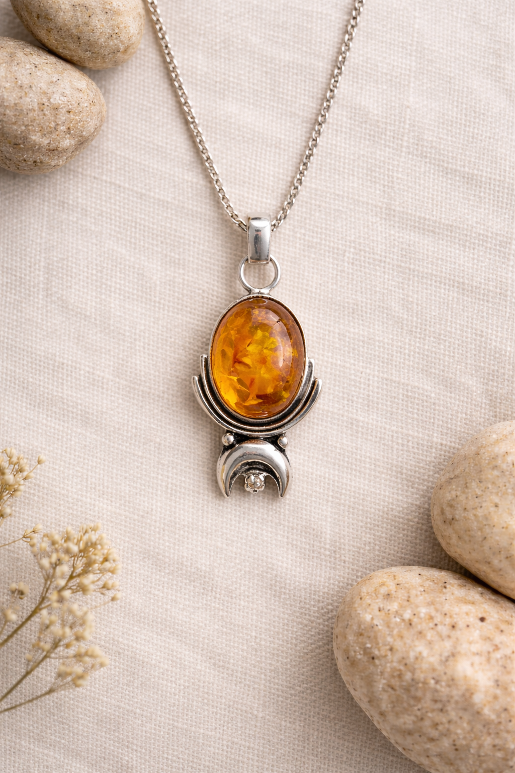 Silver necklace with an amber pendant on a beige fabric background with stones and dried flowers.