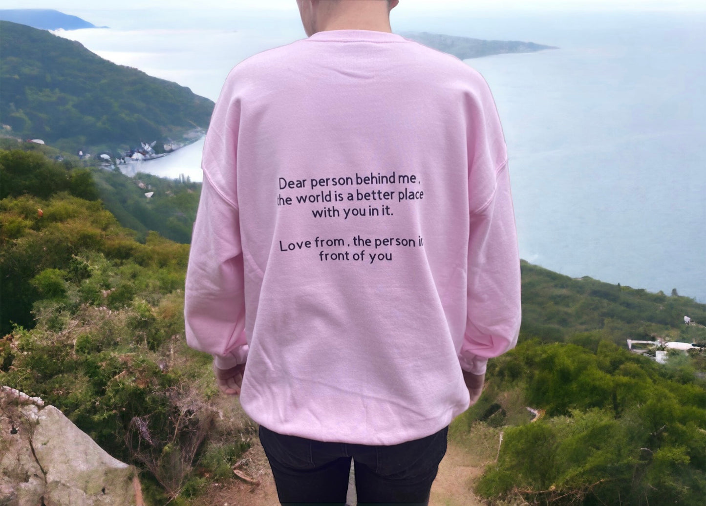 A person wearing a pink sweatshirt with a quote that reads 'Dear person behind me, the world is better with you in it.'