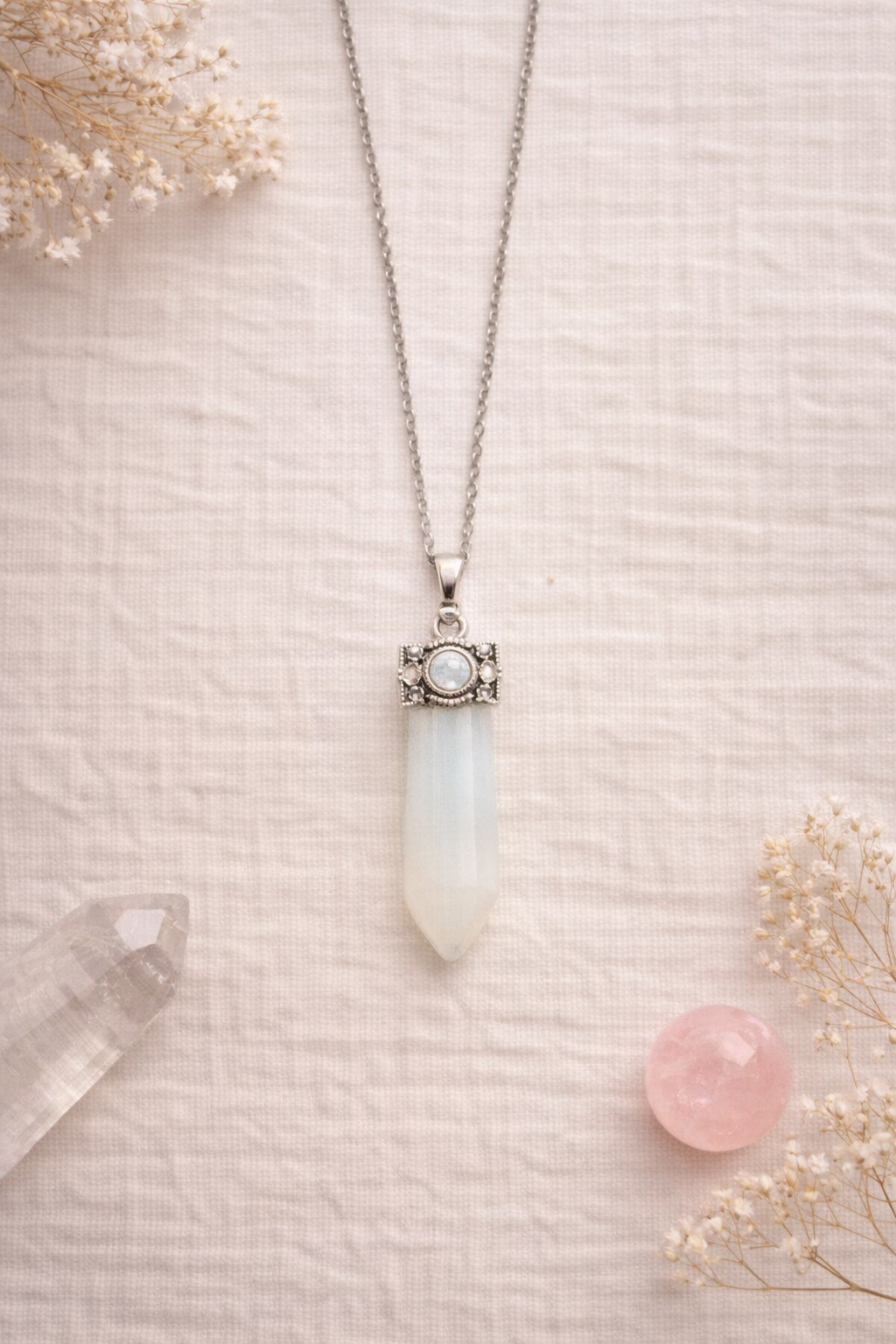 Necklace with an opaline wand pendant on a light pink background with dried flowers and a crystal.