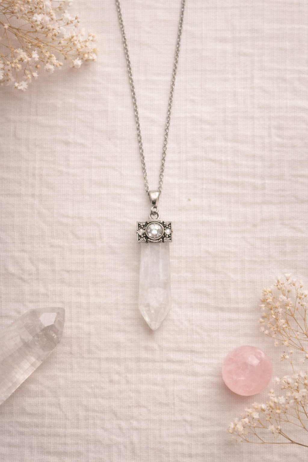 clear quartz wand  pendant necklace on a textured surface with dried flowers