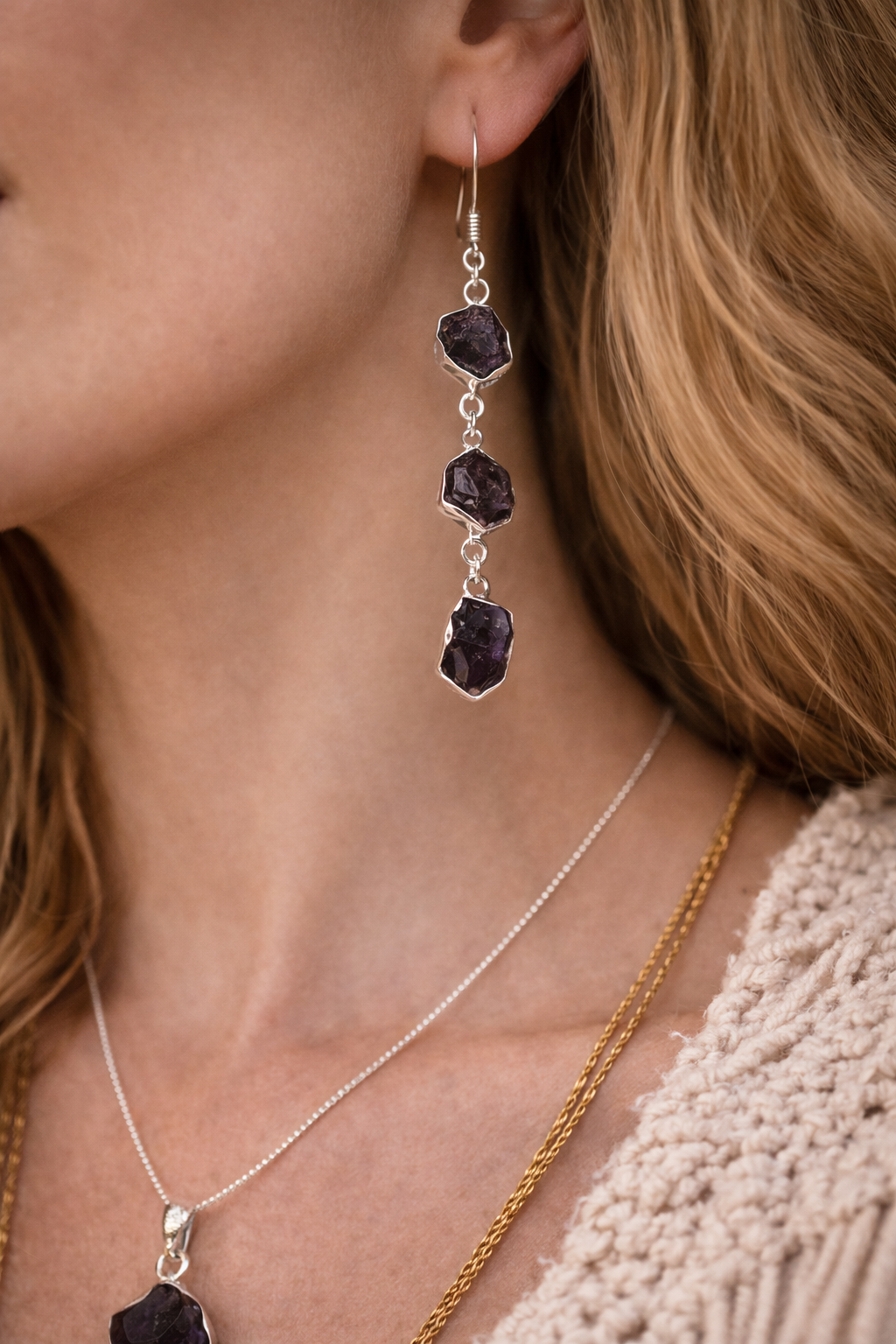 Close-up of a person wearing silver earrings with rough amethyst  gemstones 