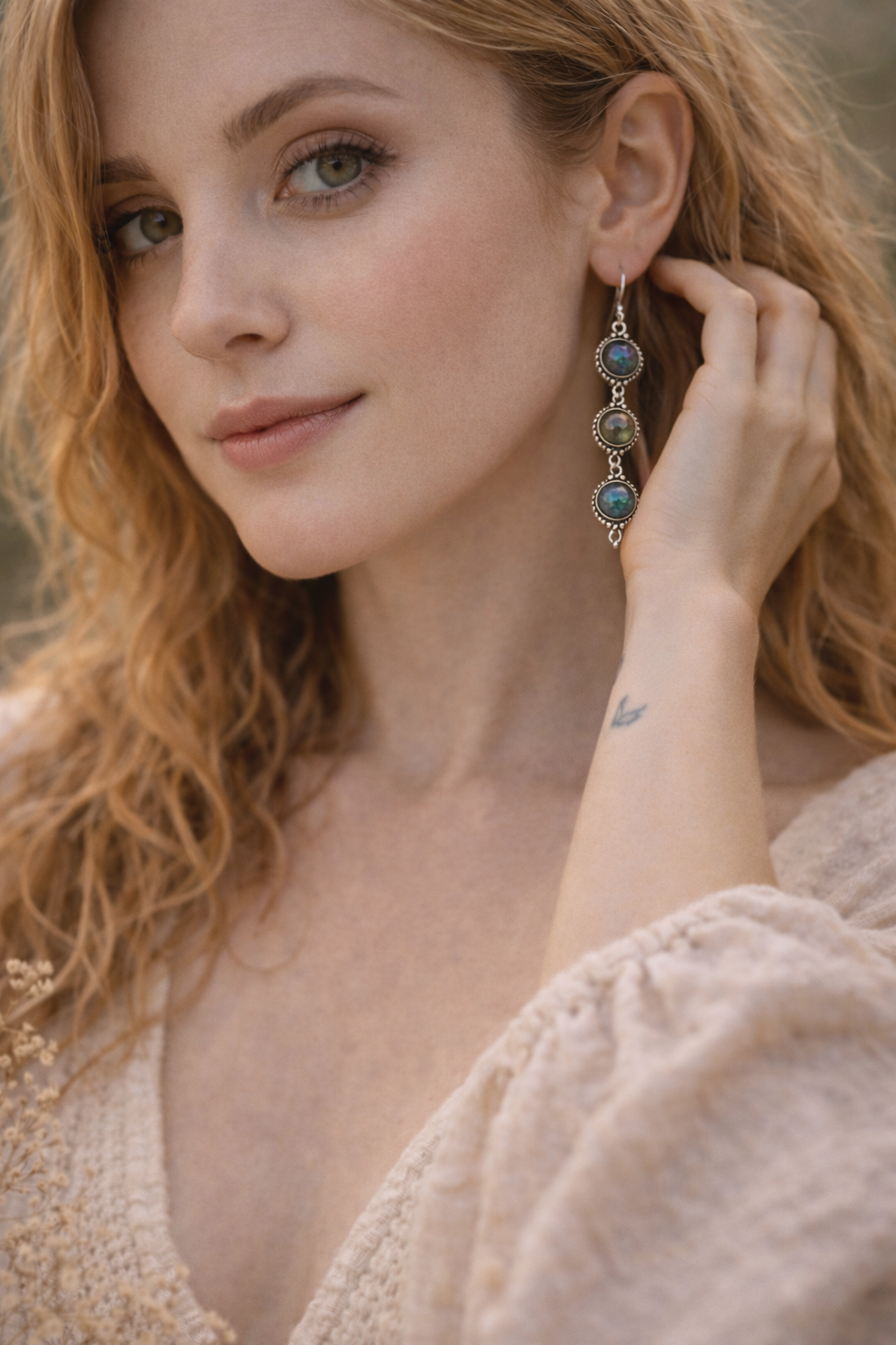 Woman wearing a pair of Labradorite earrings with blue stones, holding one ear