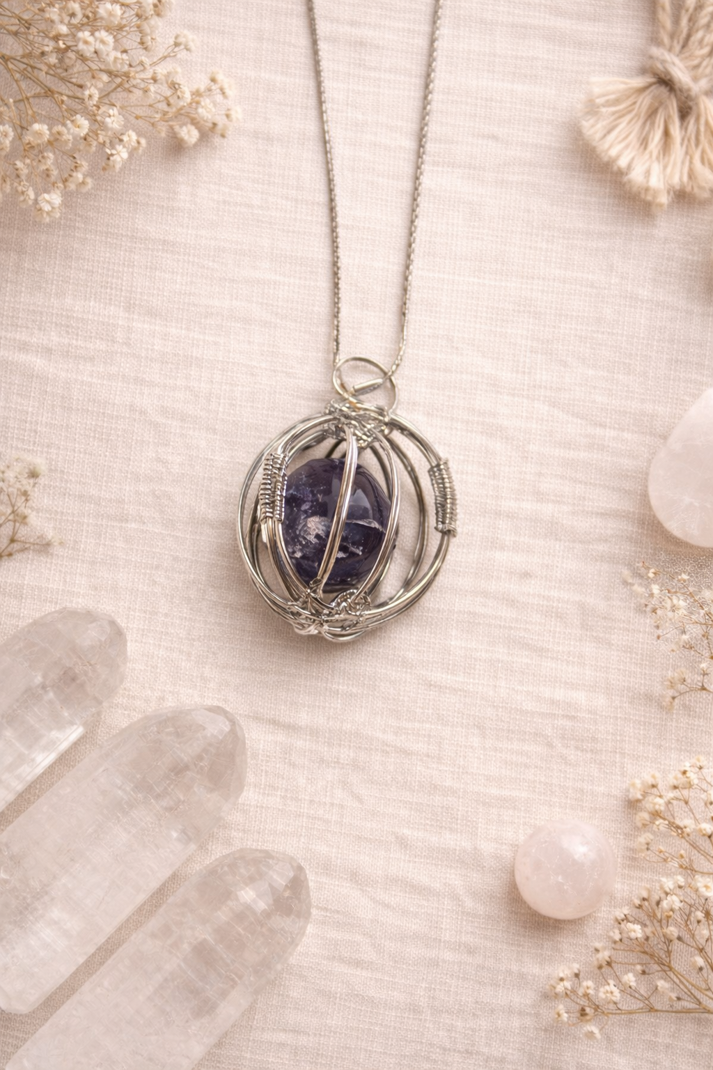 Necklace with an amethyst stone pendant in a circule cage on a textured surface with crystals and flowers.