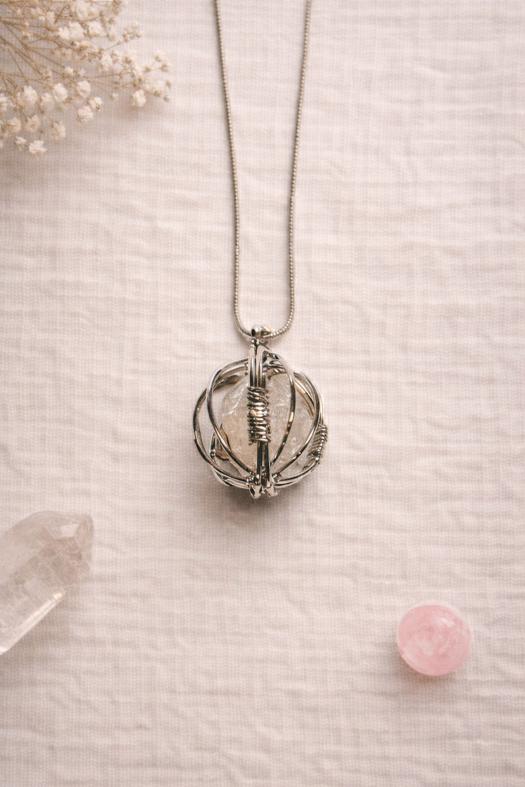 Necklace with a rose quartz crystal pendant in a circle cage on a textured surface with crystals and flowers.