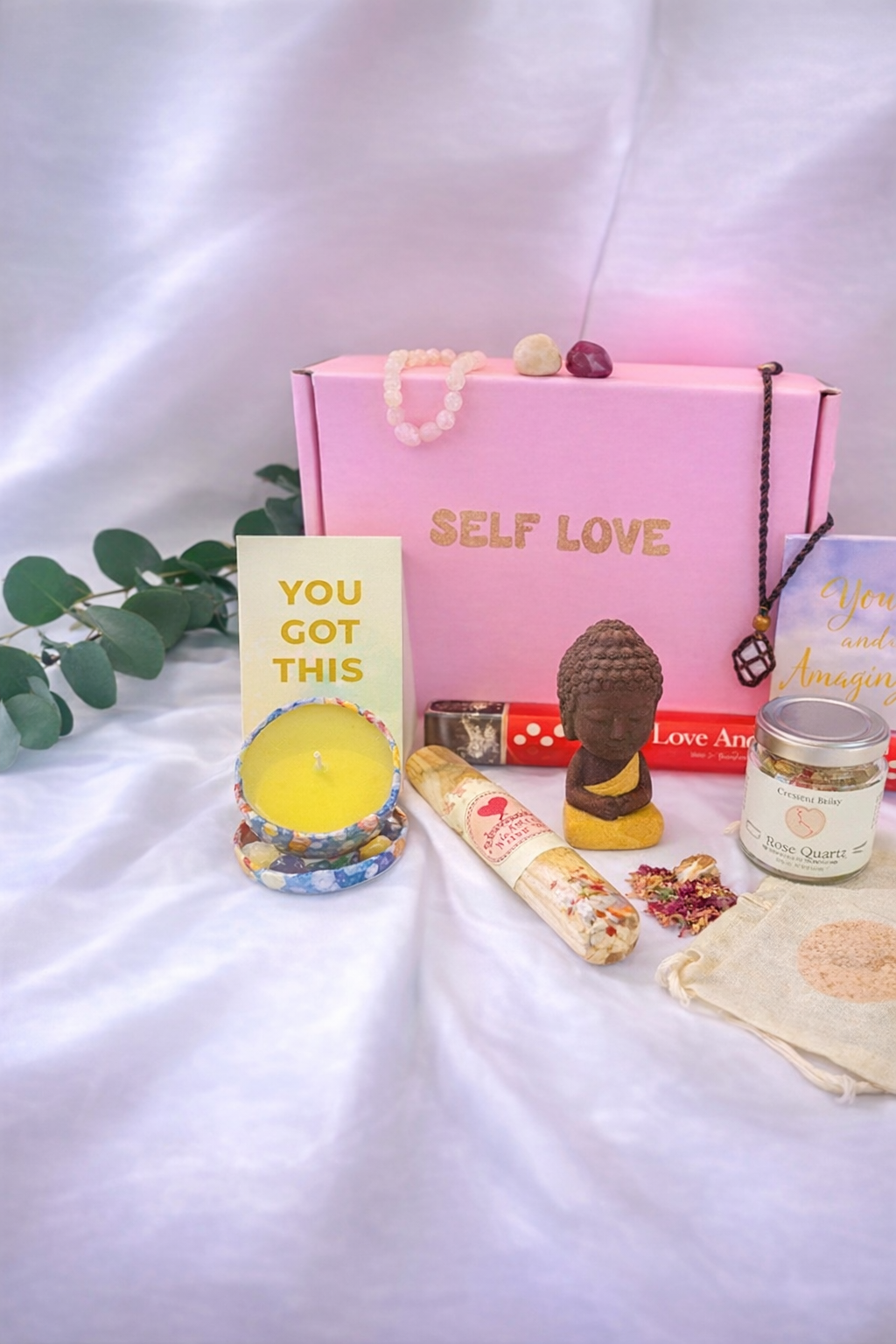 Self Love gift box with candle, crystals, affirmation cards, mini Buddha, incense, and self-care ritual items arranged on a soft white background.