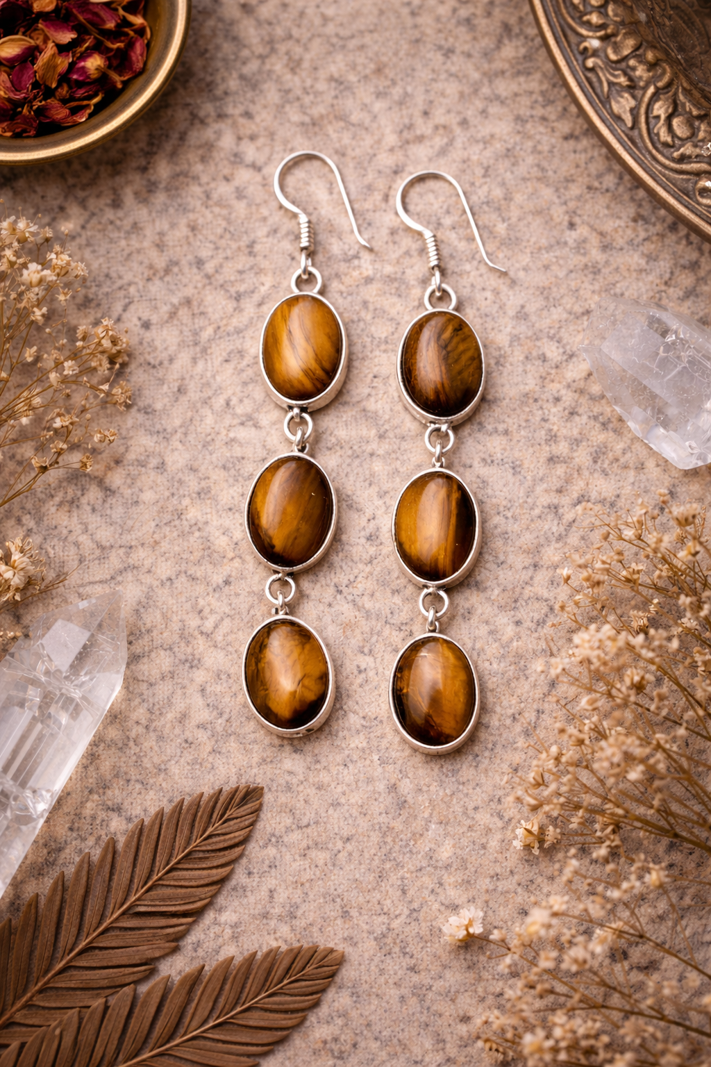 Pair of tiger eye stone earrings on a textured surface with dried flowers and leaves.