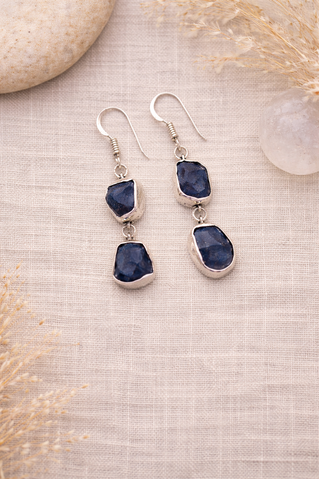 Pair of silver earrings with blue Kyanite stones on a textured beige surface