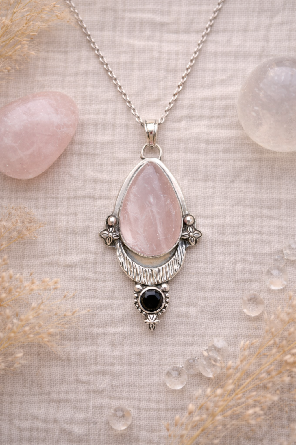 Necklace with a pink trose quartz teardrop pendant and black stone on a textured surface.