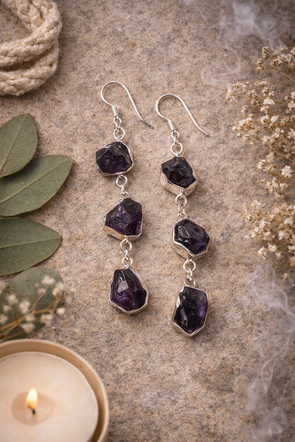 Amethyst earrings on a textured surface with leaves and a candle