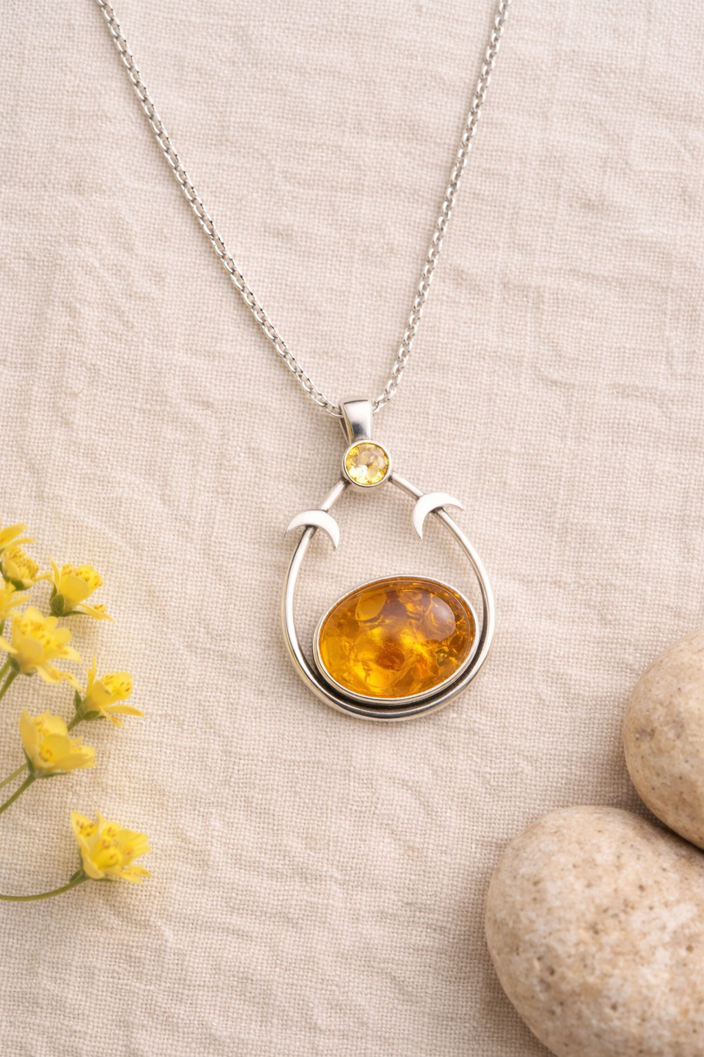 Silver necklace with amber pendant on a beige fabric background with yellow flowers and stones.