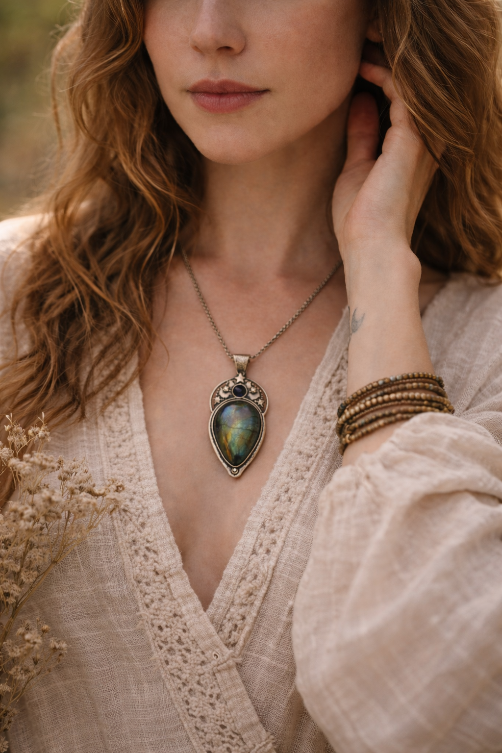 Woman wearing a necklace with a labradorite pendant and bracelets, close-up of face and upper body.