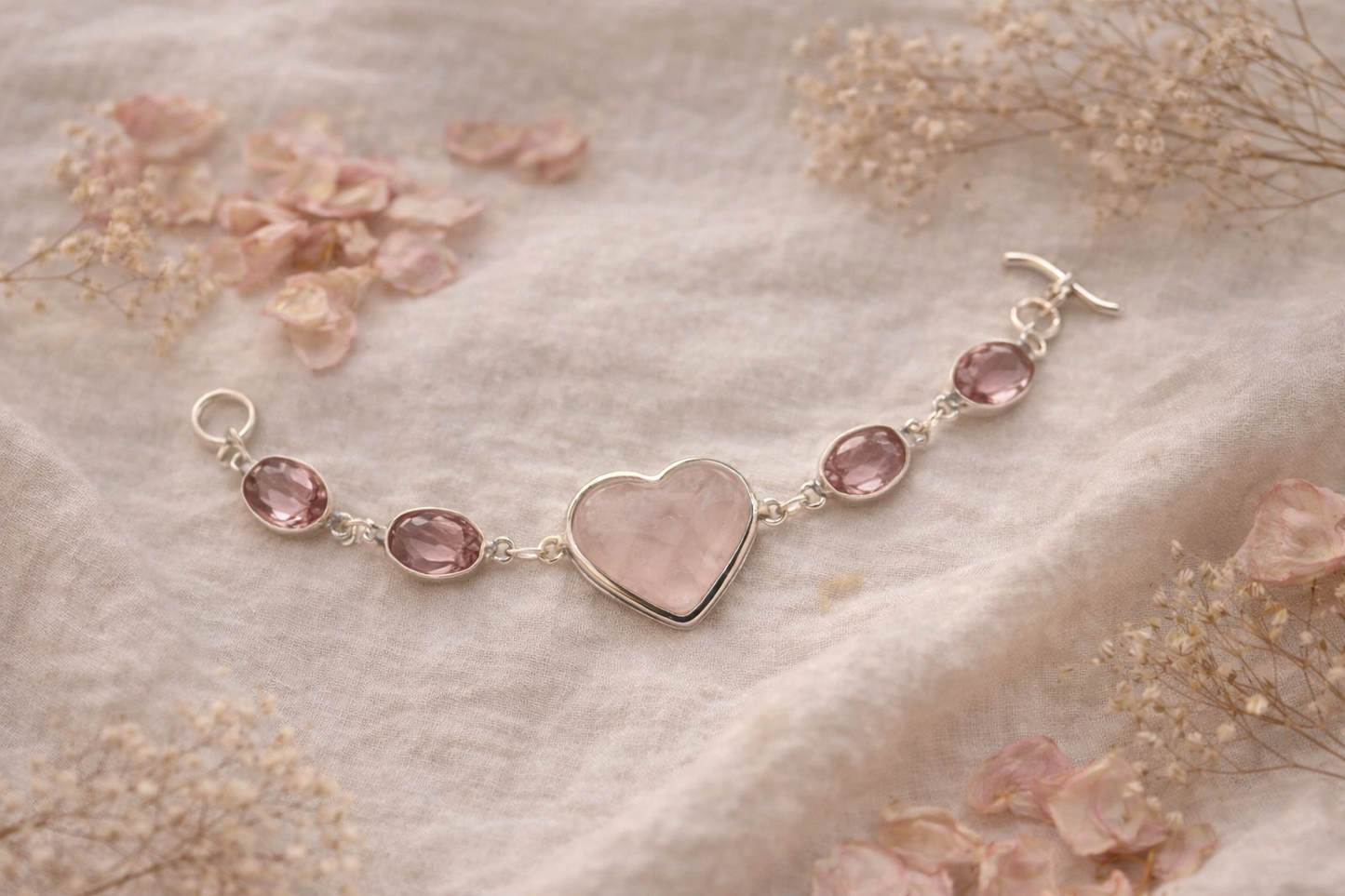 Silver bracelet with rose quartz heart charm and pink gemstones on a soft fabric background