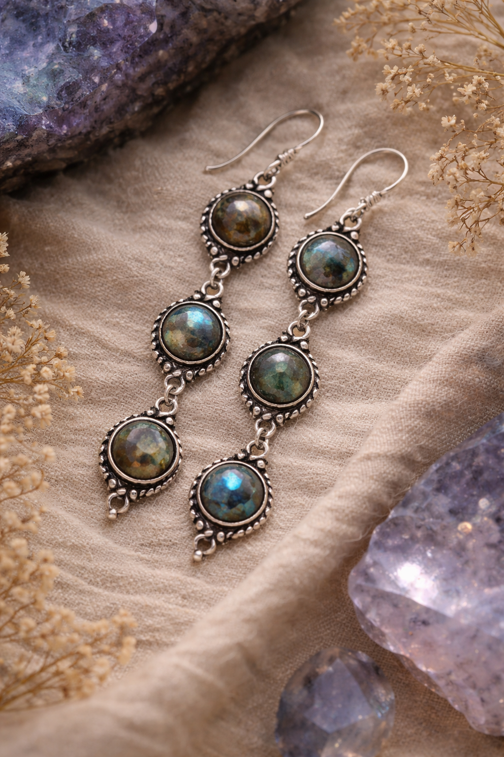 Silver earrings with labradorite stones on a textured surface with crystals.