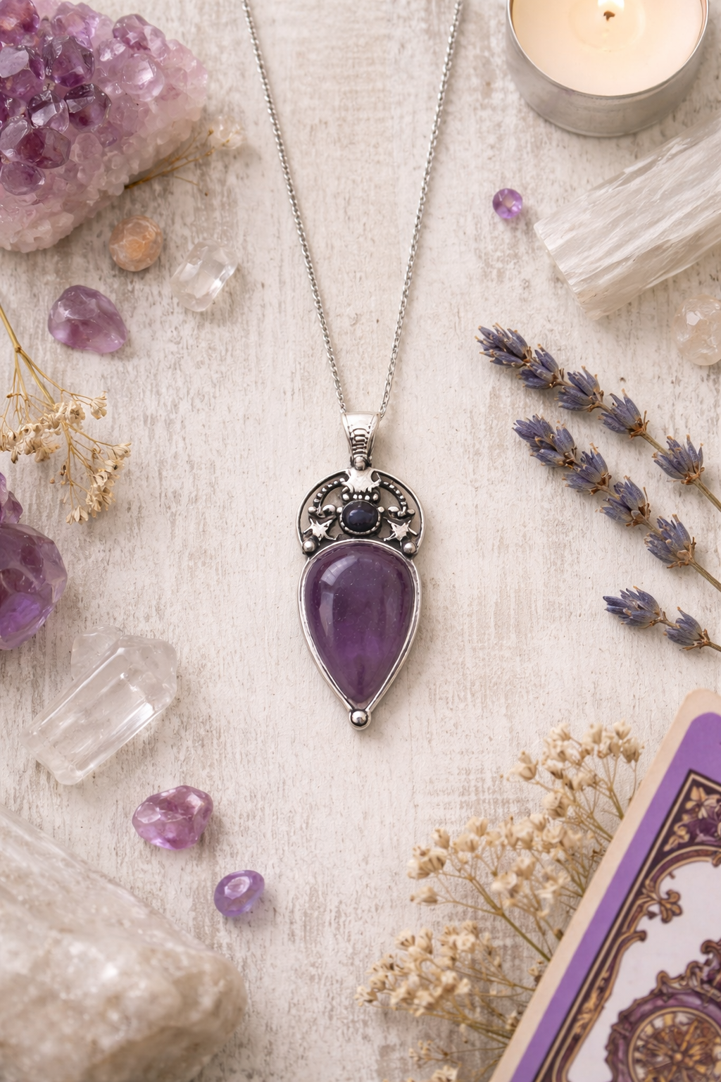 teardrop shaped amethyst pendant on white background with scattered amethyst and quartz crystals and dried flowers 