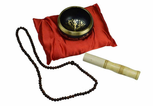 Tibetan singing bowl with meditation beads and bamboo striker on a red cushion
