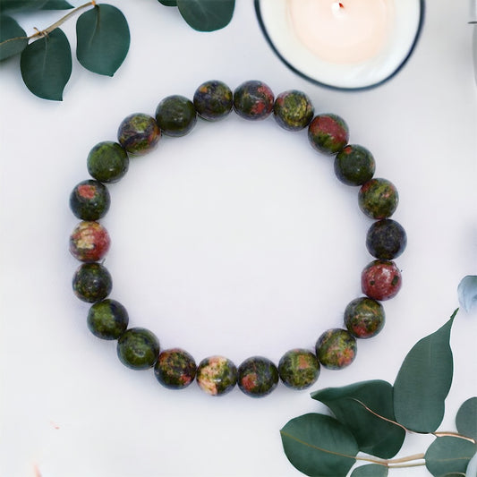 A beaded bracelet with a mix of green and red unakite stones arranged in a circle, displayed on a white background with green leaves around.