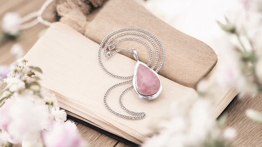 Necklace with a pink rose quartz tear drop pendant on an open book surrounded by flowers