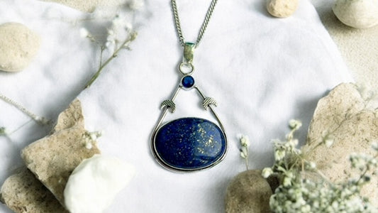 Blue Lapis Lazuli pendant necklace on a white fabric background with stones and flowers
