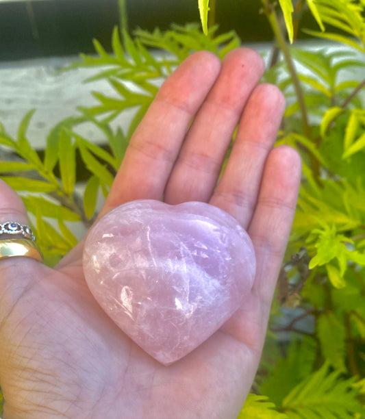 A hand holding a polished, pink rose quartz heart-shaped  5cm palm stone.